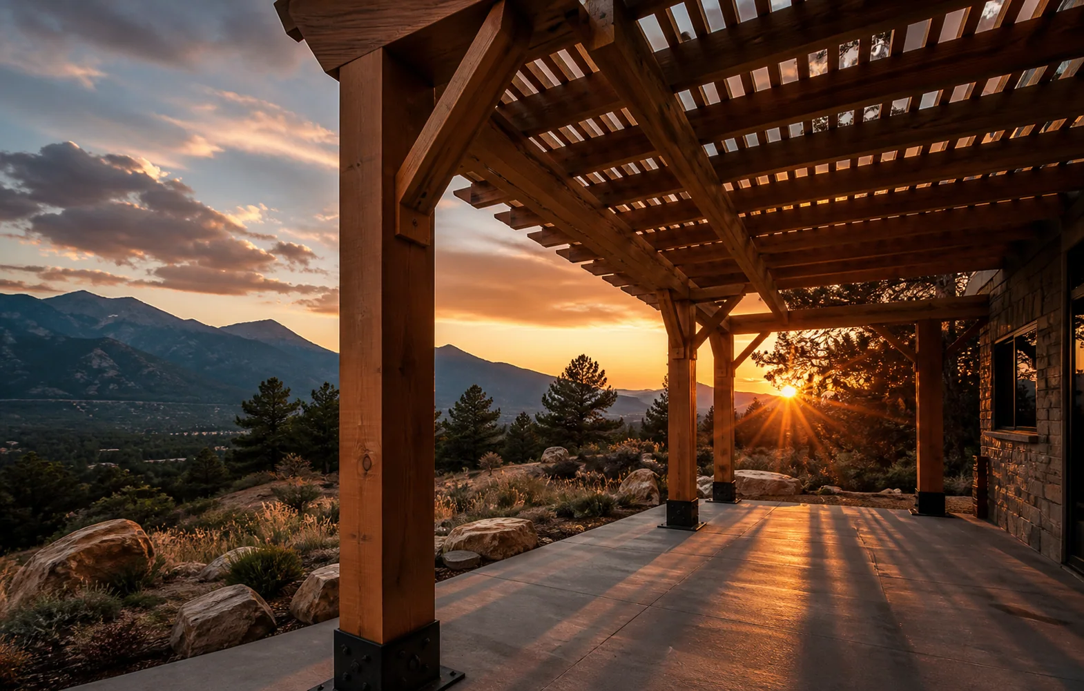 A cedar pergola anchored into a concrete patio overlooking the Front Range at sunset.